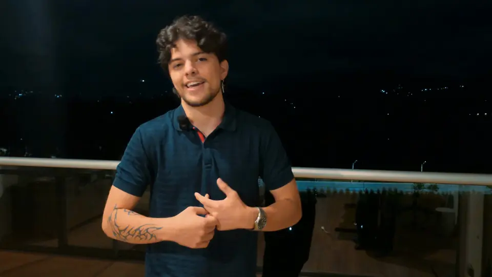 Samu sonriendo a cámara en el balcón, de noche, con la ciudad detrás